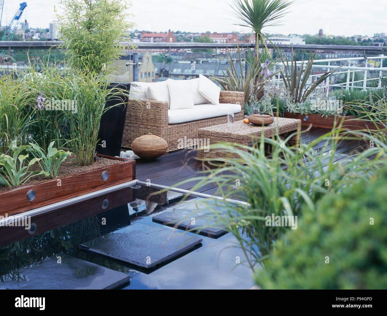 Paving slabs across pool on decked city roof garden with raised beds and seagrass table and sofa Stock Photo