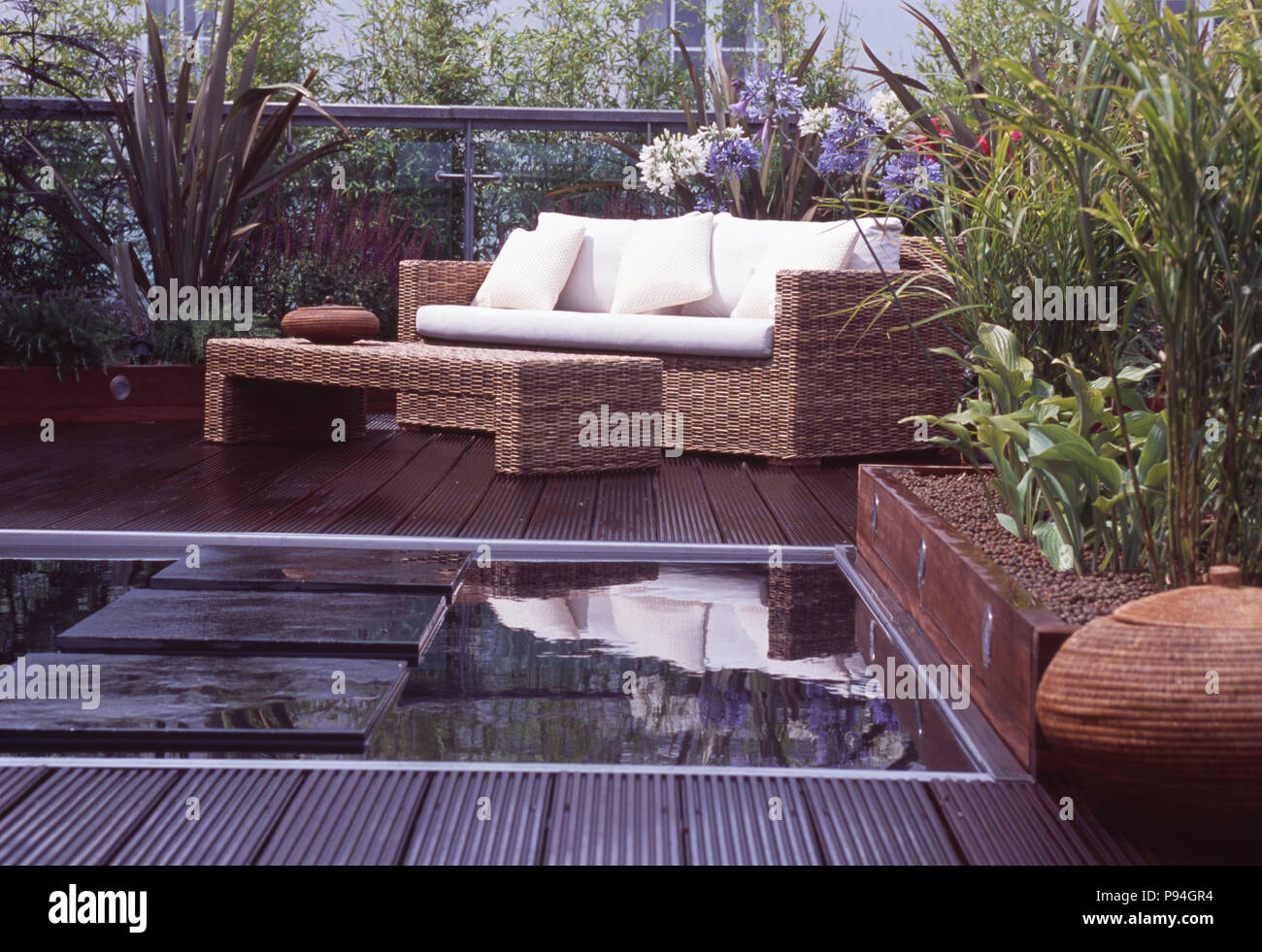 Lushly planted roof garden with seagrass table and sofa with white cushions on decking beside pool with stone paving Stock Photo