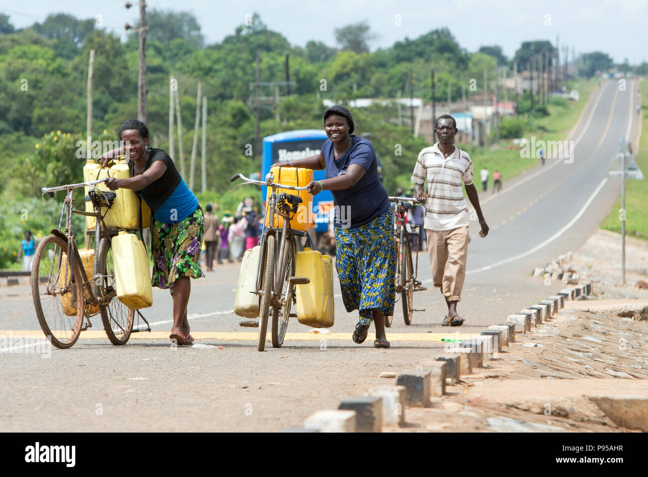 Kamdini, Uganda - city view. Two women push up a hill, carrying bicycles laden with plastic canisters. Stock Photo