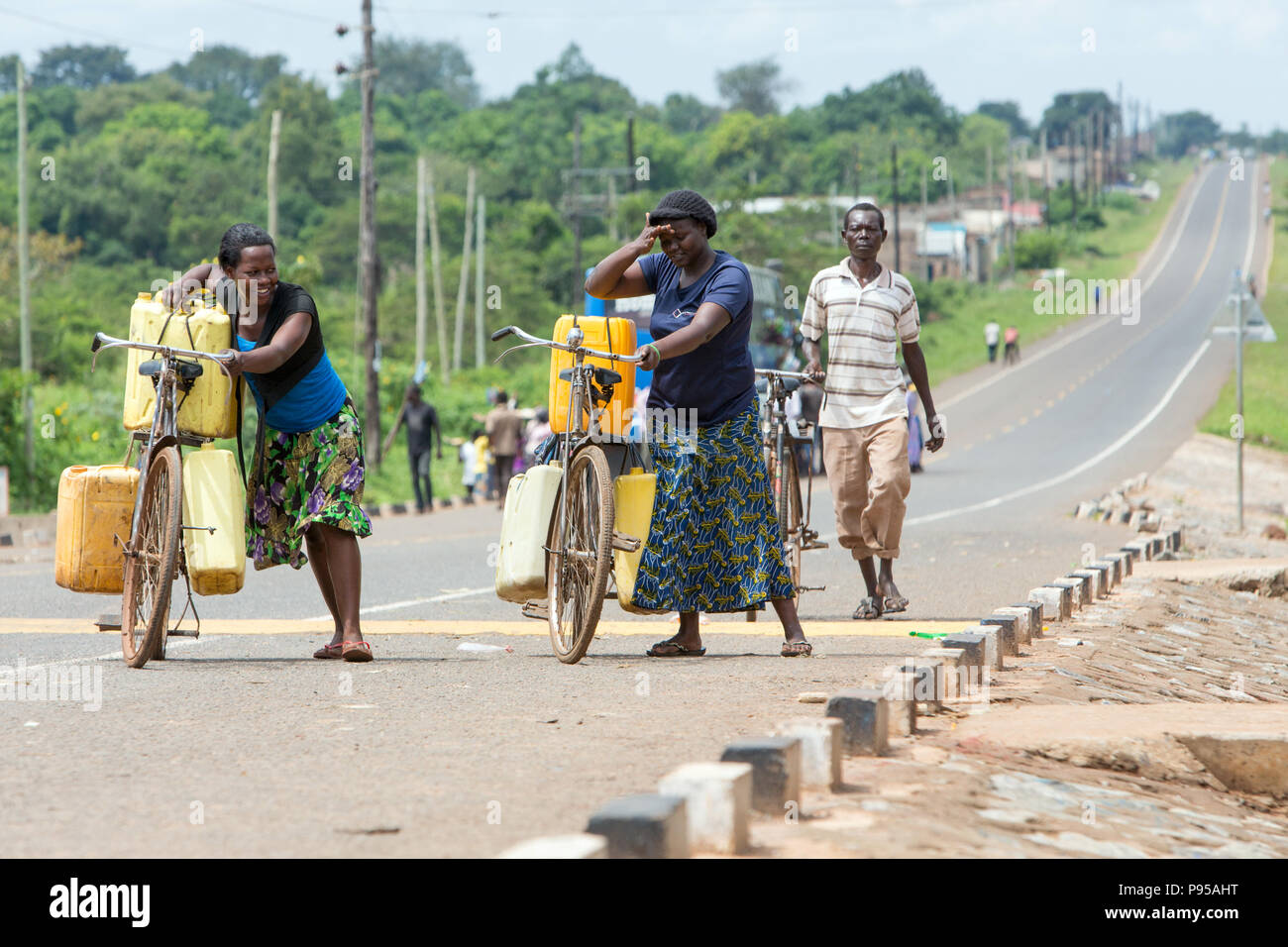 Kamdini, Uganda - city view. Two women push up a hill, carrying bicycles laden with plastic canisters. Stock Photo