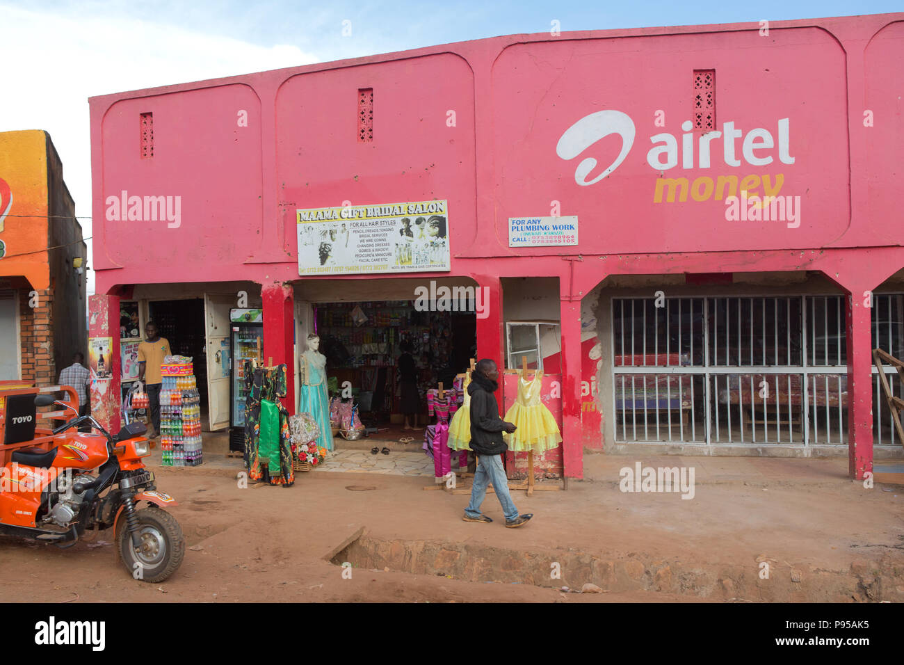 Wakiso Town, Uganda - Street scene. Store shops. A man walks past a pink colored women's boutique. Stock Photo
