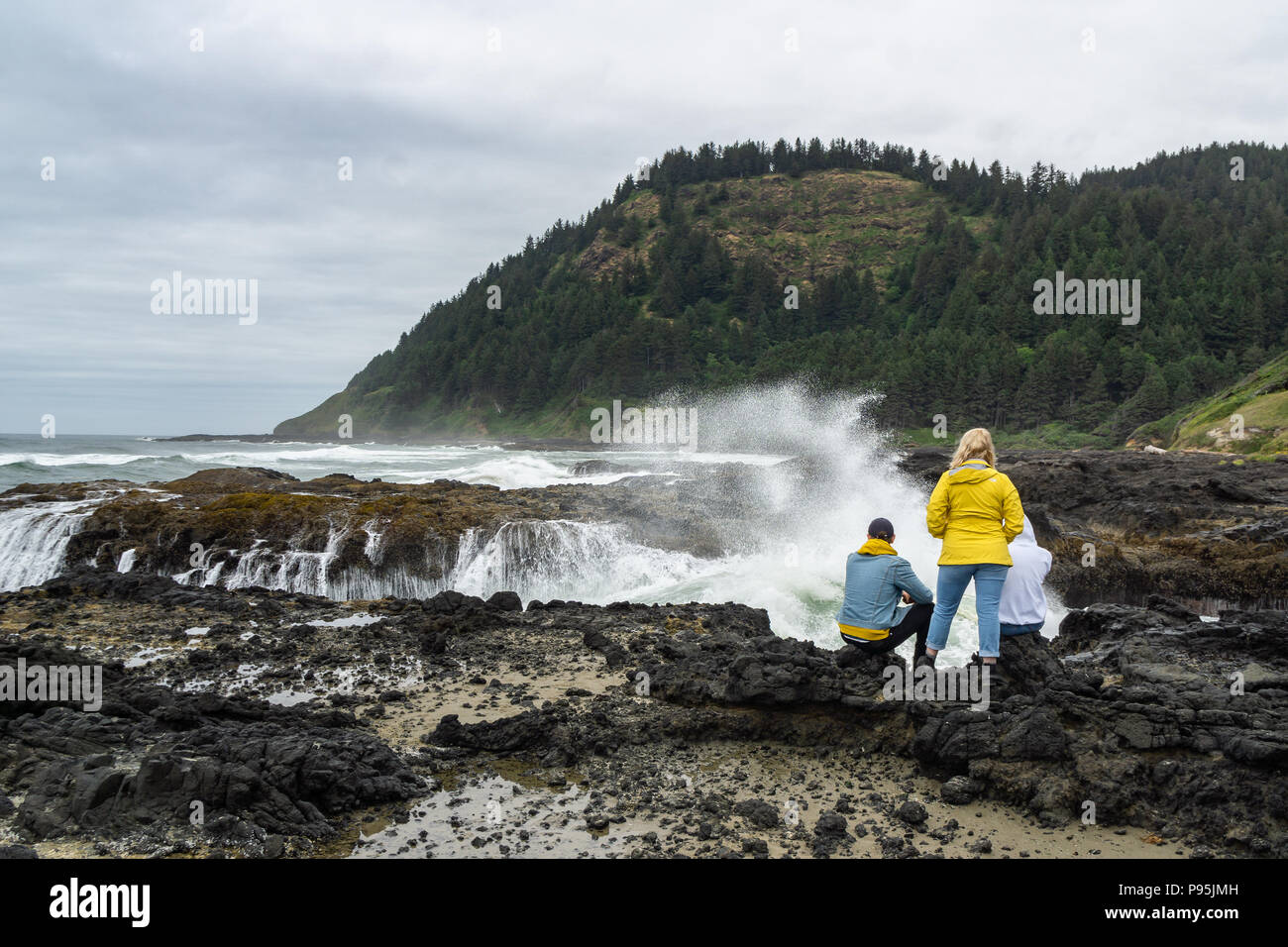 Young people enjoying basaltic headland of Cape Perpetua Scenic Area watching waves crashing in a churn, Oregon Coast, USA. Stock Photo