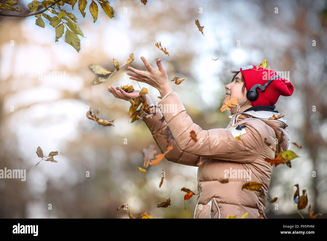 Happy girl with Red cap walks in autumn Park and catches the falling leaves Stock Photo