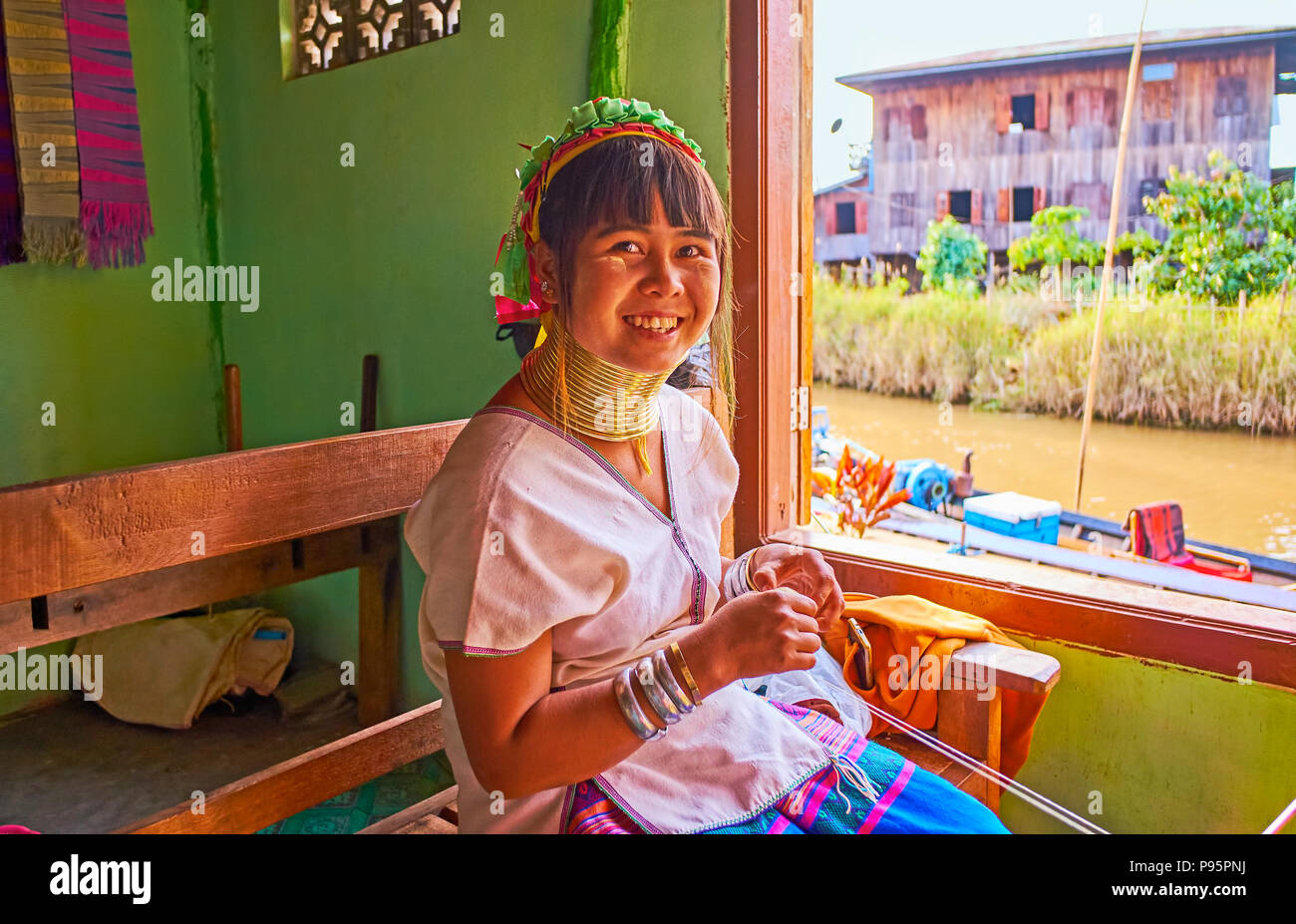 INLE LAKE, MYANMAR - FEBRUARY 18, 2018: The portrait of young smiling Padaung Kayan woman with brass rings on the neck, she works in traditional text Stock Photo