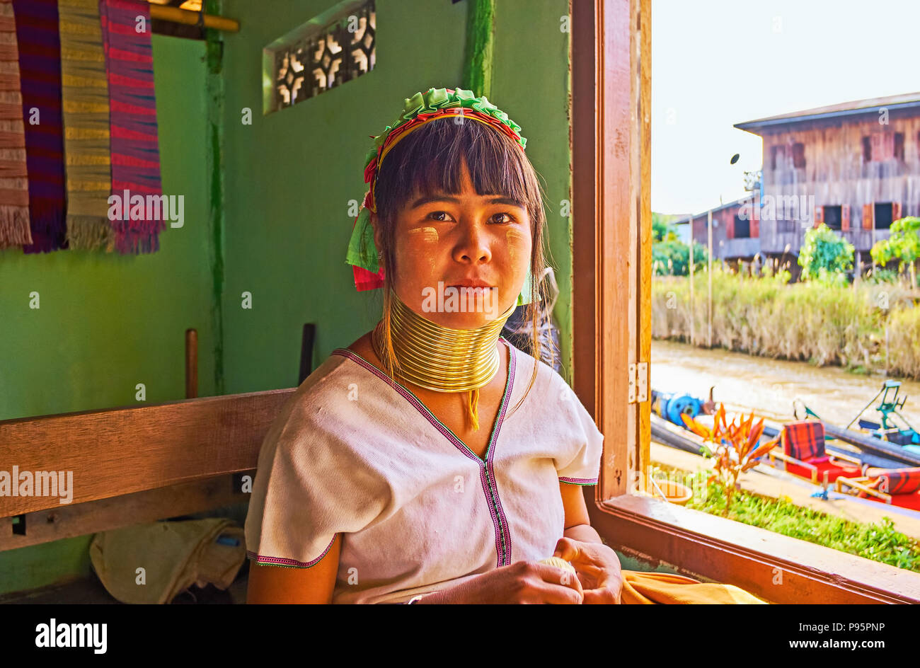 INLE LAKE, MYANMAR - FEBRUARY 18, 2018: The portrait of Padaung Kayan long neck woman, sitting at the window of the workshop, on February 18 on Inle Stock Photo