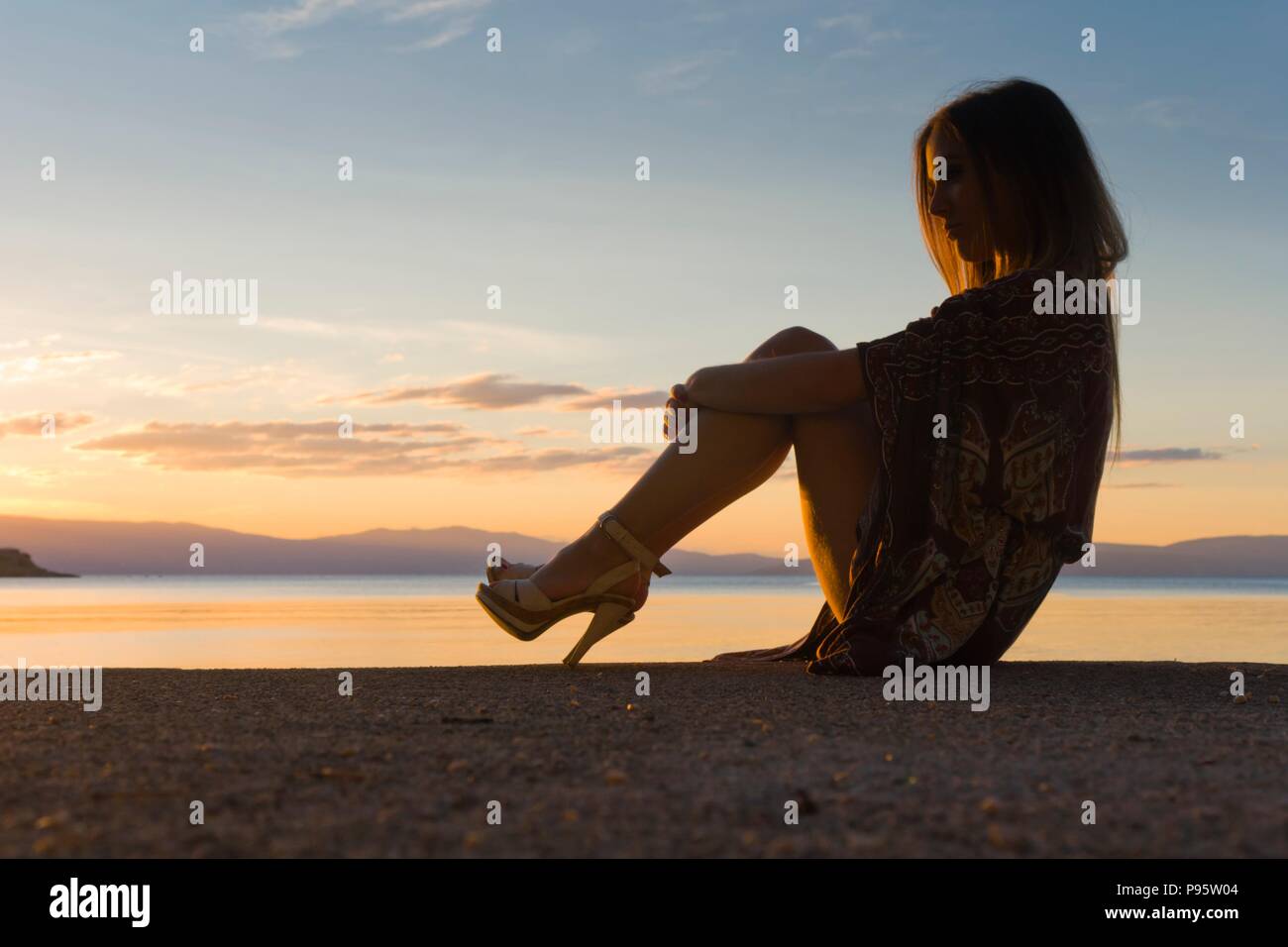 Heelsaddiced heelsaddict young woman person on seaside near sea in evening sunset time romantic serenity warm low light horizon island MR Stock Photo