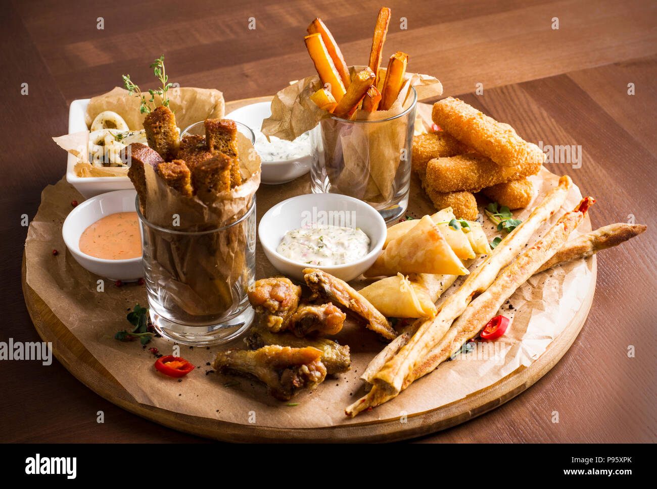 different beer snacks calamari rings fries hot wings bread and sauces on wooden board P95XPK