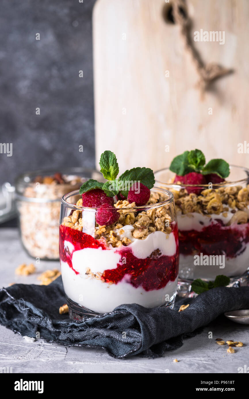 Healthy layered dessert with yogurt, granola, jam and raspberries in glass. Stock Photo