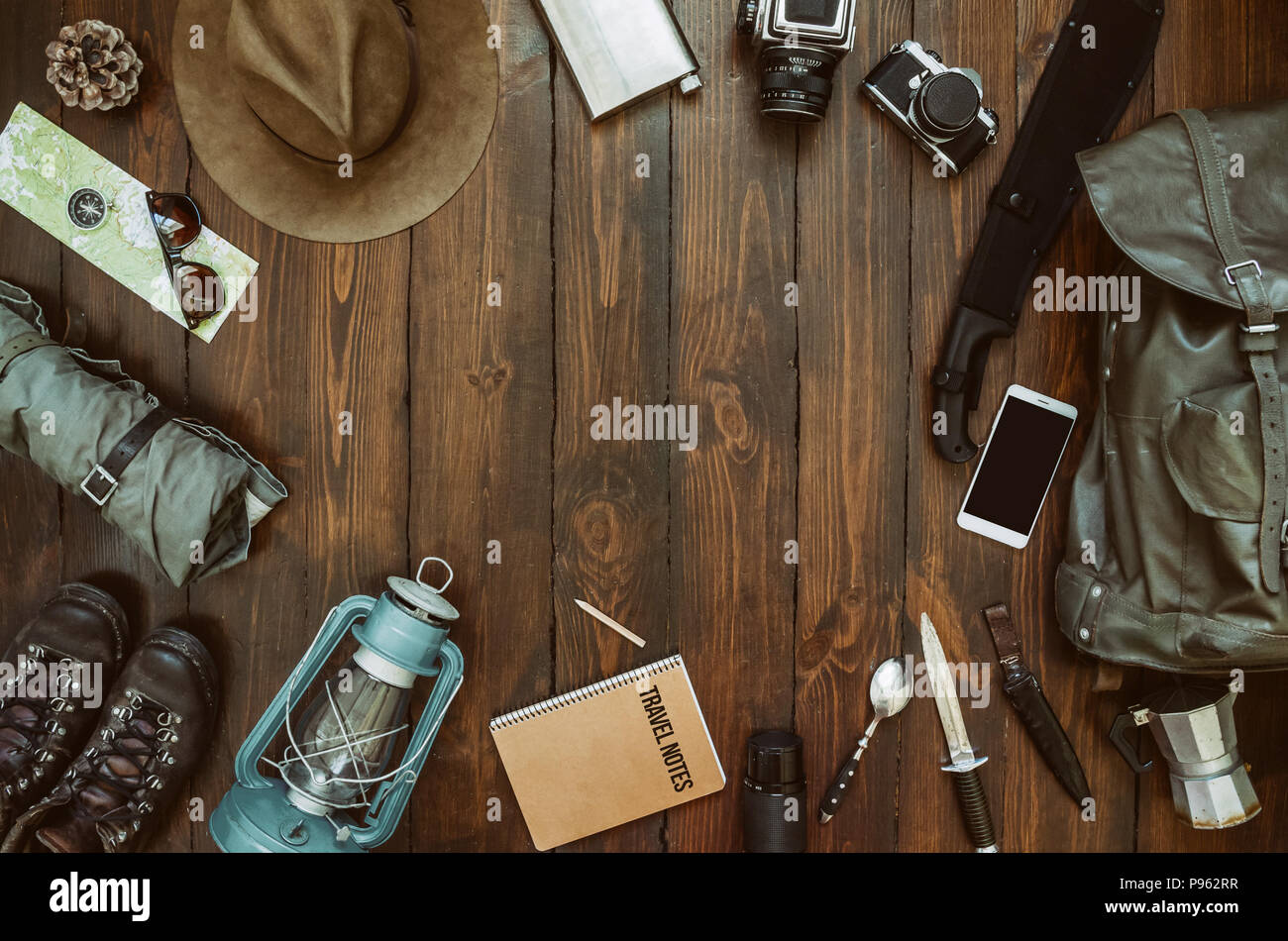 Hiking gear frame including machete, knife, clothes, boots, lantern, camera, hat, map, compass, mobile phone. Wanderlust, safari postcard, poster. Stock Photo