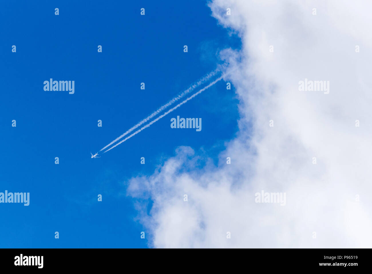 Jet vapour trail in blue sky with white clouds Stock Photo