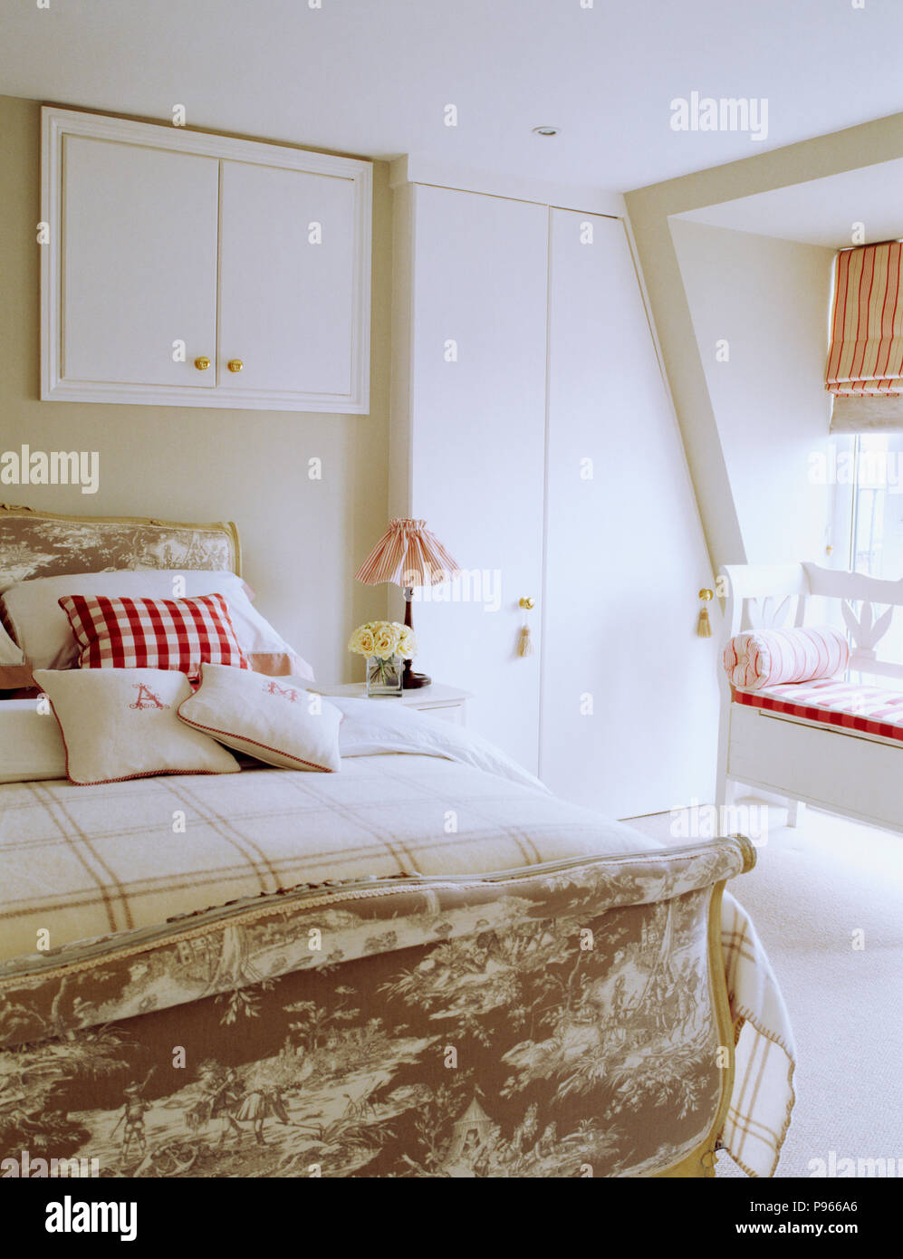 Monogrammed and checked linen cushions on Toile-de-Jouy upholstered French-style bed in white loft bedroom Stock Photo