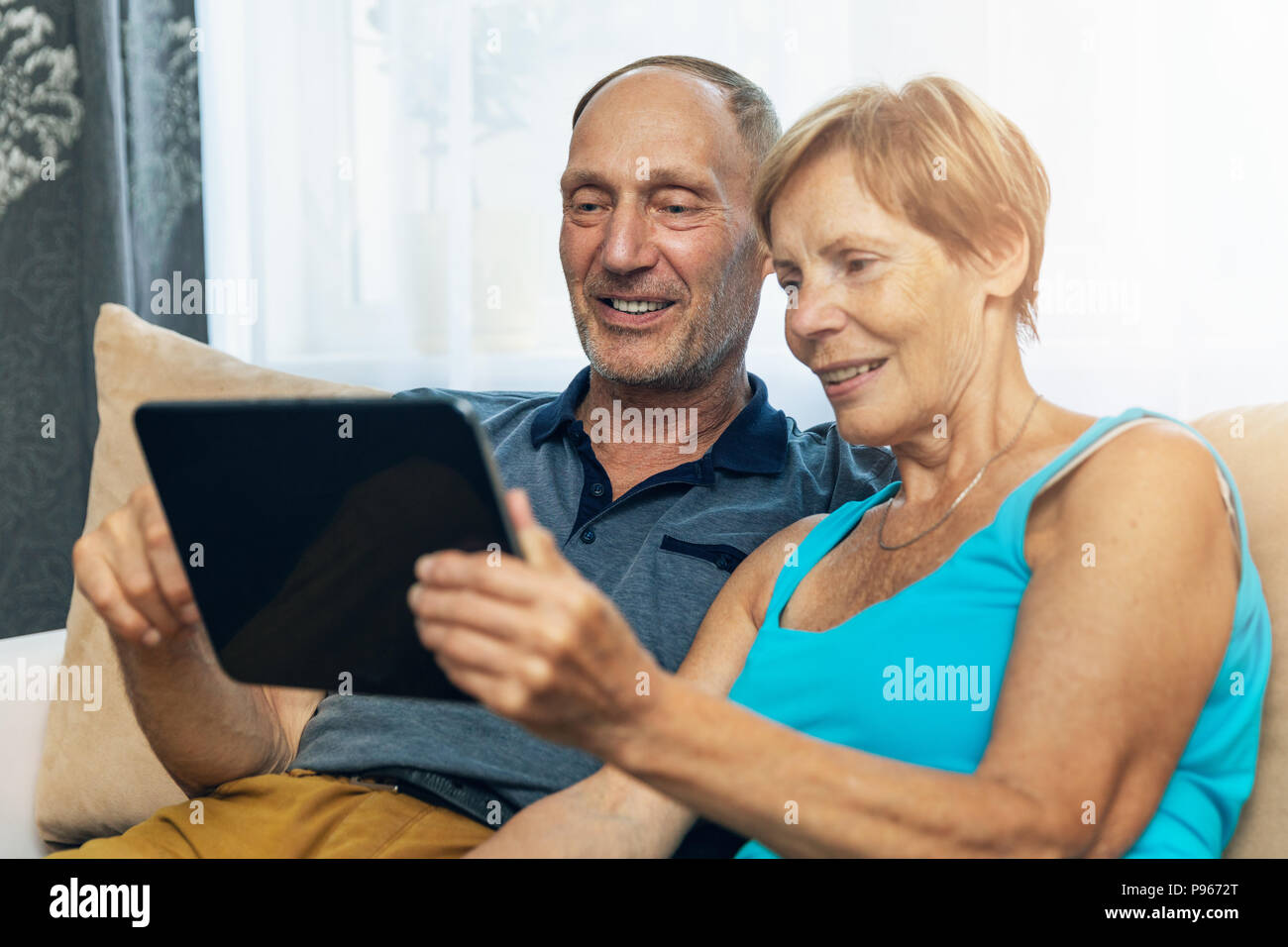happy senior couple sitting on couch and using digital tablet at home Stock Photo