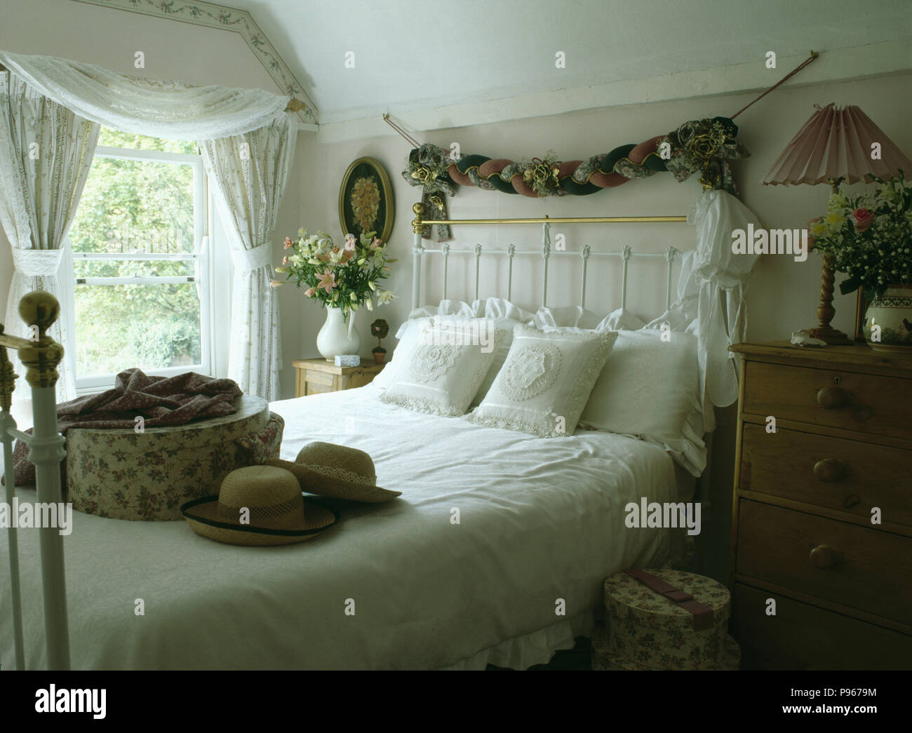 Fabric garland above white wrought-iron and brass bed with hatbox and hats on the bed Stock Photo