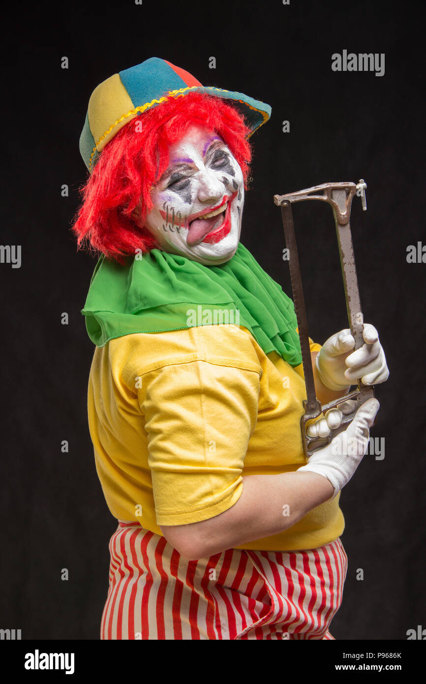 Scary evil clown with an ugly smile and saw on a black backgroun Stock
