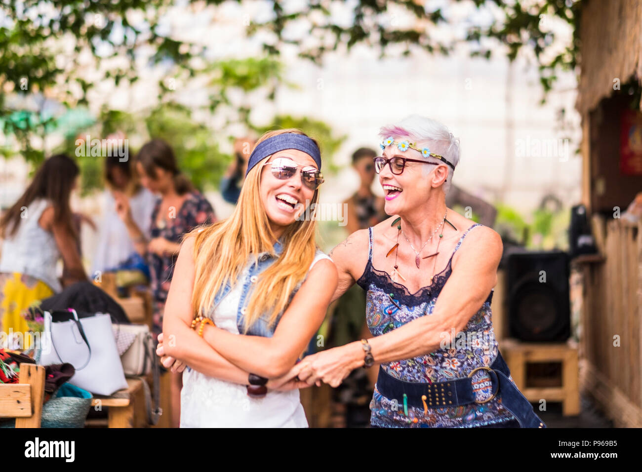 happy friendship couple of woman young and mature ladies with hippy clothes and dress have fun together dancing and hugging each other. beautiful adul Stock Photo