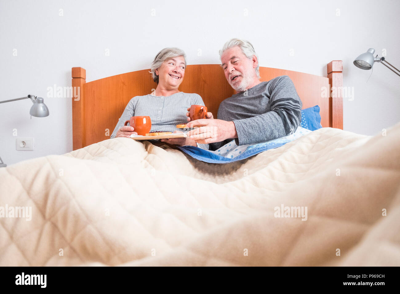 caucasian aged couple doing breakfast at home in the bed. nice natural scene at home for togheterness life concept. love and carefree people married.  Stock Photo