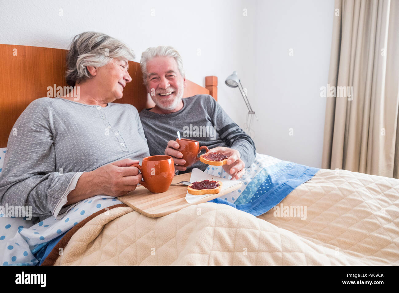 nice caucasian aged senior couple enjoying and laughing together waking up in the early morning. toasted and marmelade and coffee. togetherness and fo Stock Photo