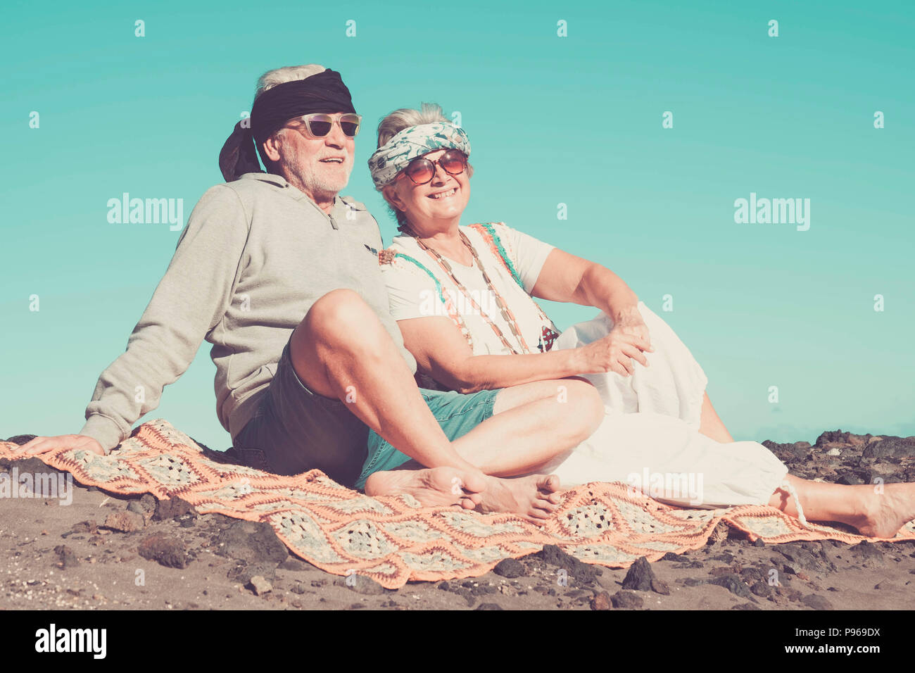 couple of senior caucasian hippy style and life rest on the rocky beach in tenerife. colors and alternative lifestyle for totally freedom concept near Stock Photo