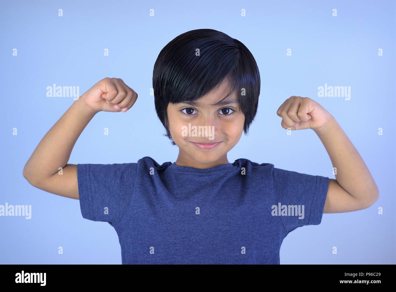 Portrait of young boy smiling looking at camera. Smart kid showing his arms muscles with fists Stock Photo