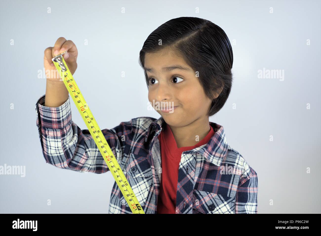 Kid using measuring tape. Smiling kid looking at numbers on tape measure. Concept of measuring height or growing tall. Stock Photo