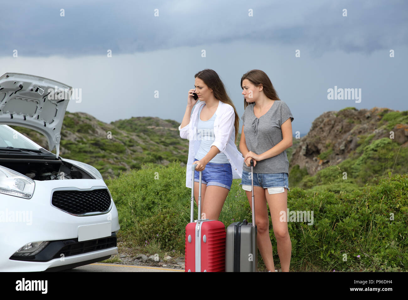 Frustrated tourists calling insurance about a brokendown car looking at the opened hood Stock Photo