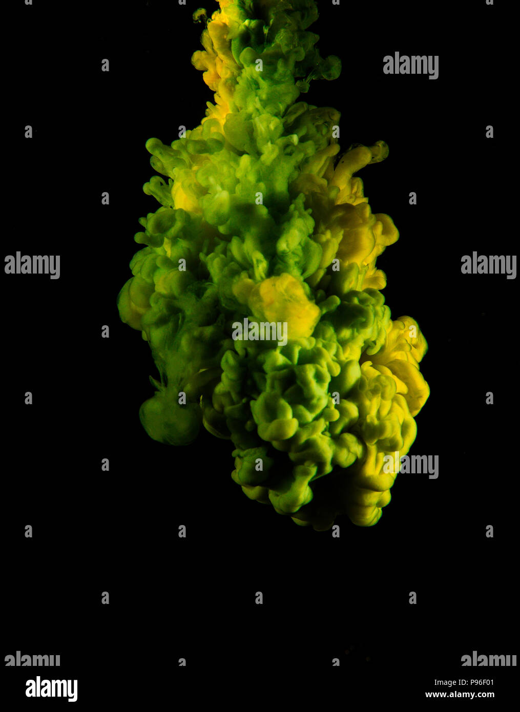 Yellow and Green ink dropping into an abyssal black background and spreading into clouds. Stock Photo