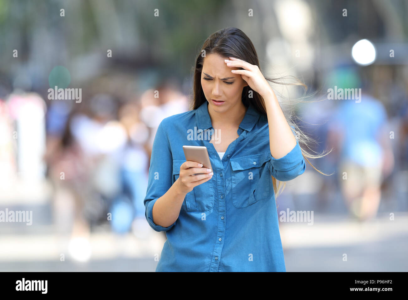 Front view portrait of a worried woman checking smart phone messages walking on the street Stock Photo