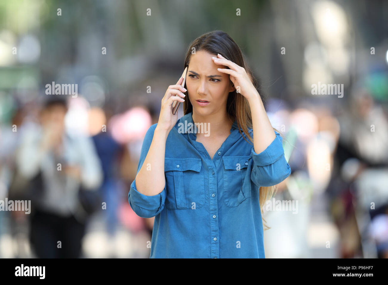 Fronf view of a worried woman talks on the phone walking in the street Stock Photo