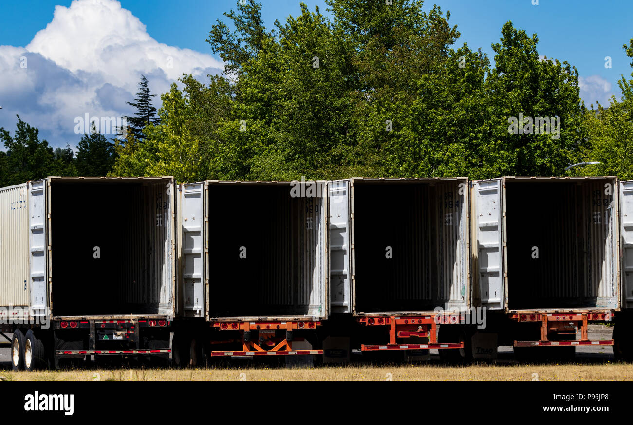 Semi tractor trailers empty and open parked in a lot with trees and brown grass Stock Photo