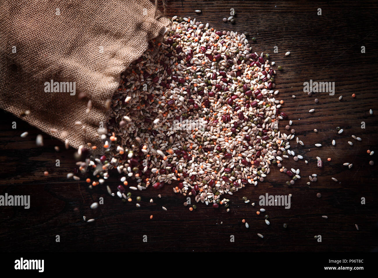 Jute sack pouring barley and other cereals on the wooden table. Stock Photo