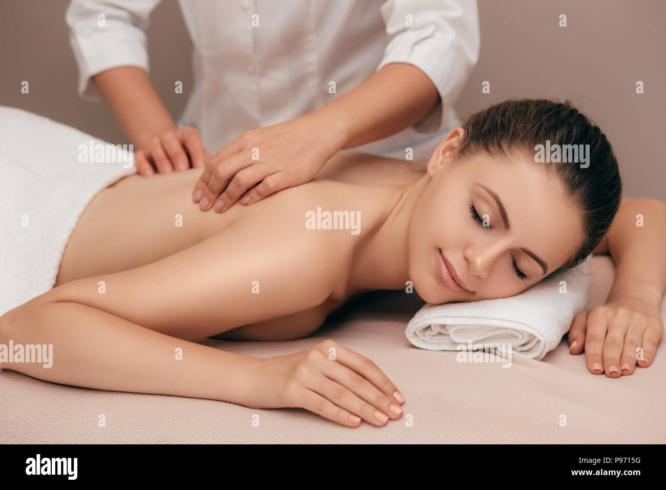 Young smiling woman receiving back massage from a massage professional at beauty salon Stock Photo