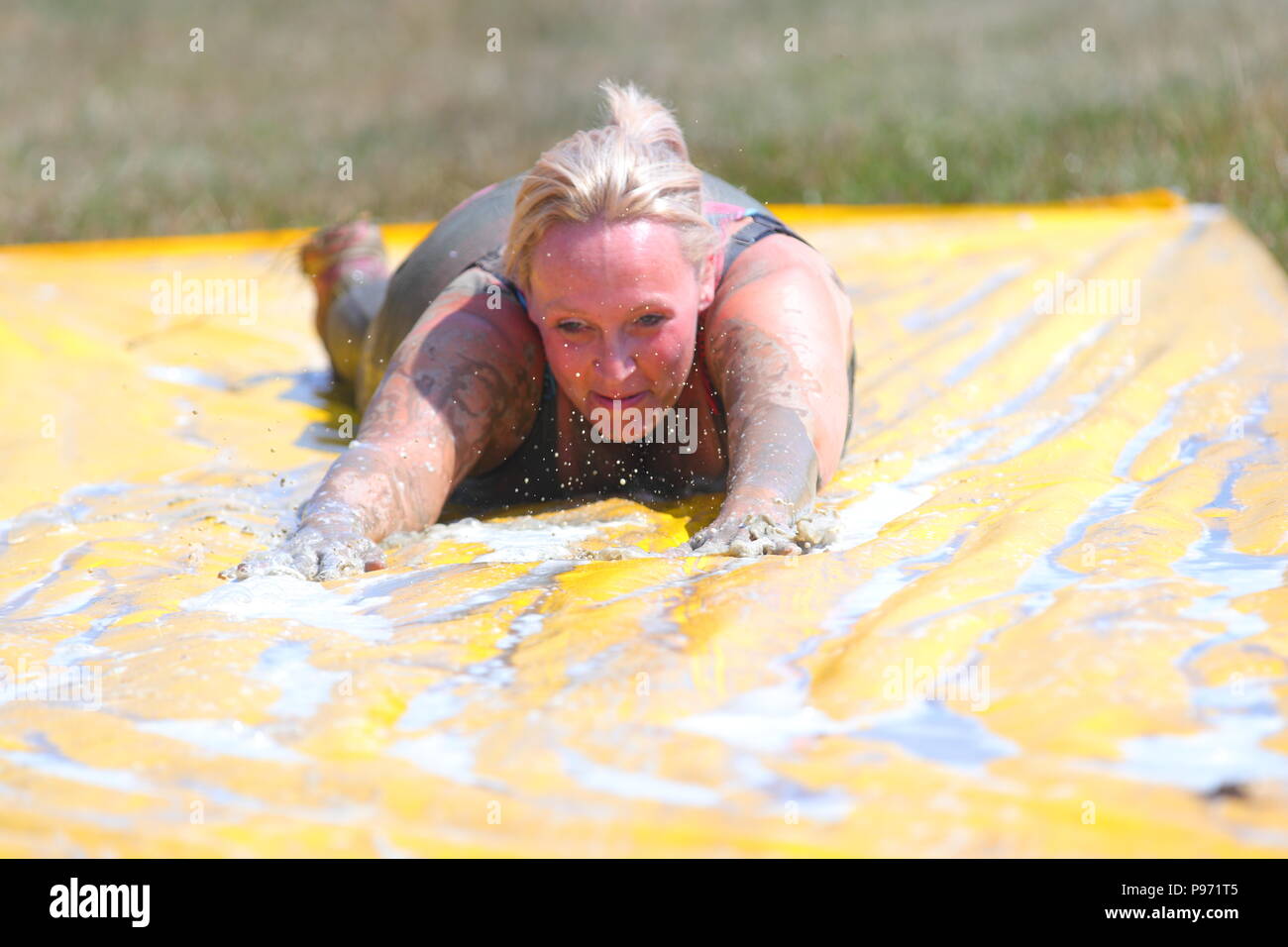 A woman slides down a muddy slide which is one of many muddy obstacles during the Young Mudders event in Leeds. Stock Photo
