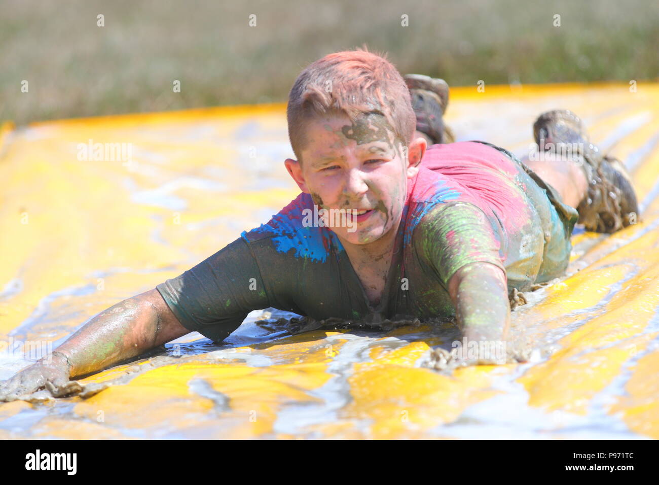 A young boy having fun on a mud slide and one of many obstacles during a Young Mudders event which is a 2.5k & 5k muddy obstacle course. Stock Photo