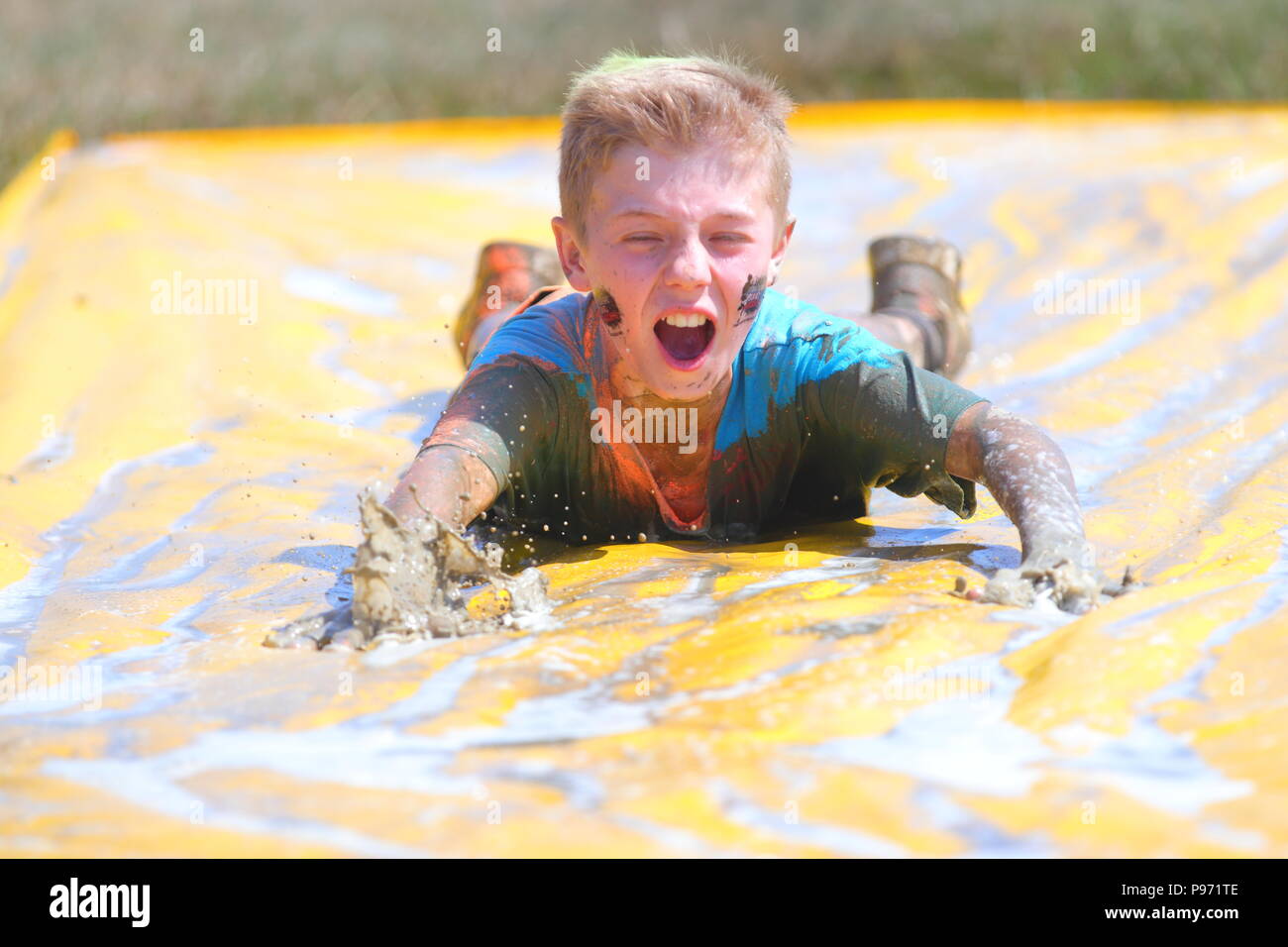 A young boy having fun on a mud slide and one of many obstacles during a Young Mudders event which is a 2.5k & 5k muddy obstacle course. Stock Photo