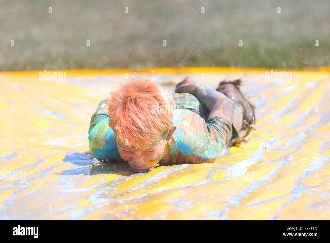 A young boy having fun on a mud slide and one of many obstacles during a Young Mudders event which is a 2.5k & 5k muddy obstacle course. Stock Photo