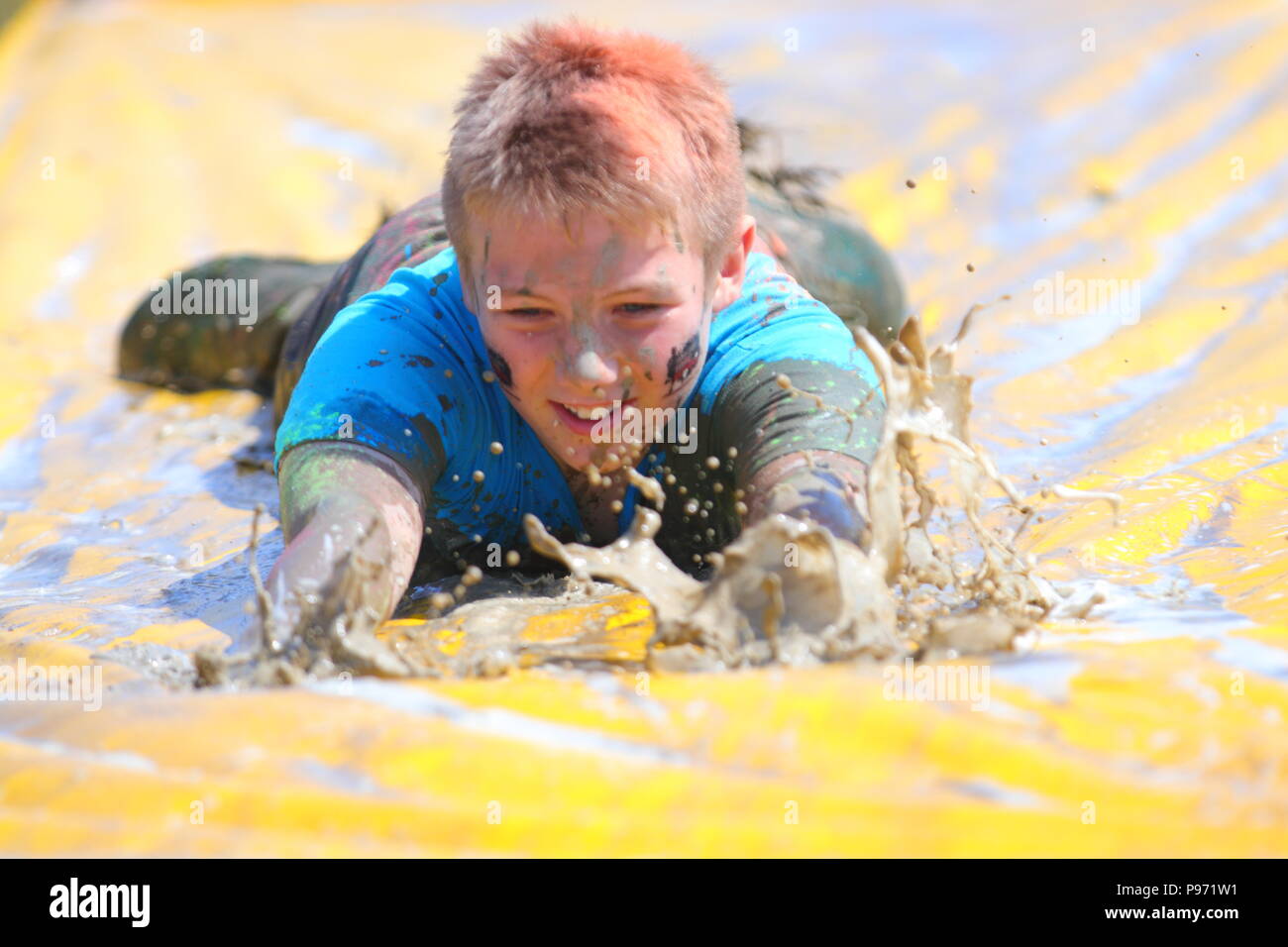 A young boy having fun on a mud slide and one of many obstacles during a Young Mudders event which is a 2.5k & 5k muddy obstacle course. Stock Photo