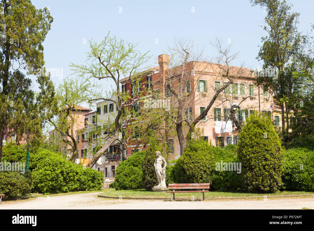Statue in the Giardini Pubblici or Public Gardens, Castello, Venice, Veneto, italy in spring with a bench, greenery and trees backed by historic build Stock Photo