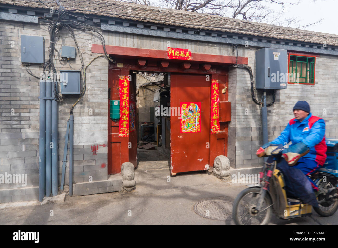 Man riding a motorcyle in a hutong in Beijing. Hutongs are narrow alleys in traditional Chinese residential areas and a Stock Photo