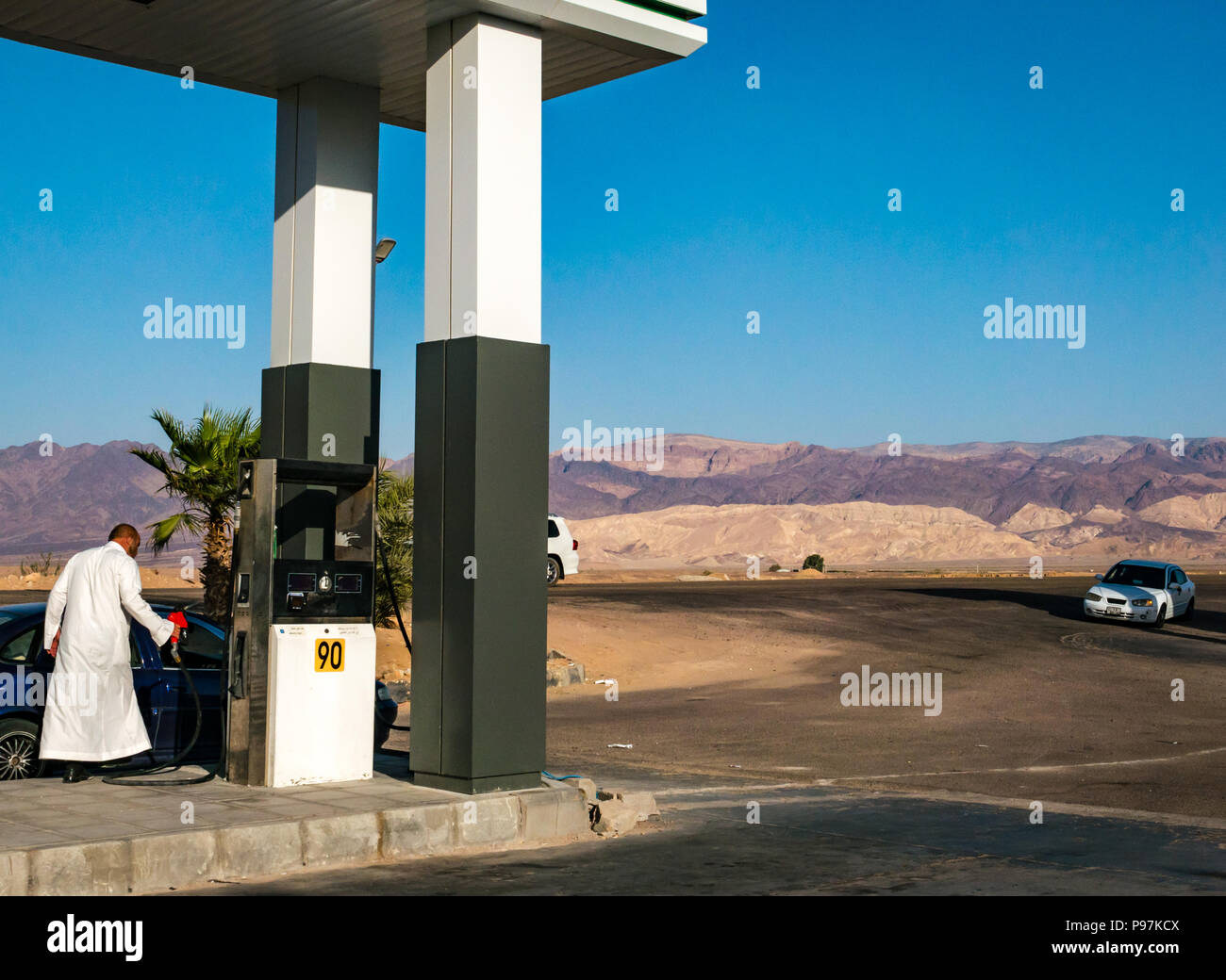 Man in traditional white robe filling car with petrol at desert highway filling station, Jordan, Middle East Stock Photo