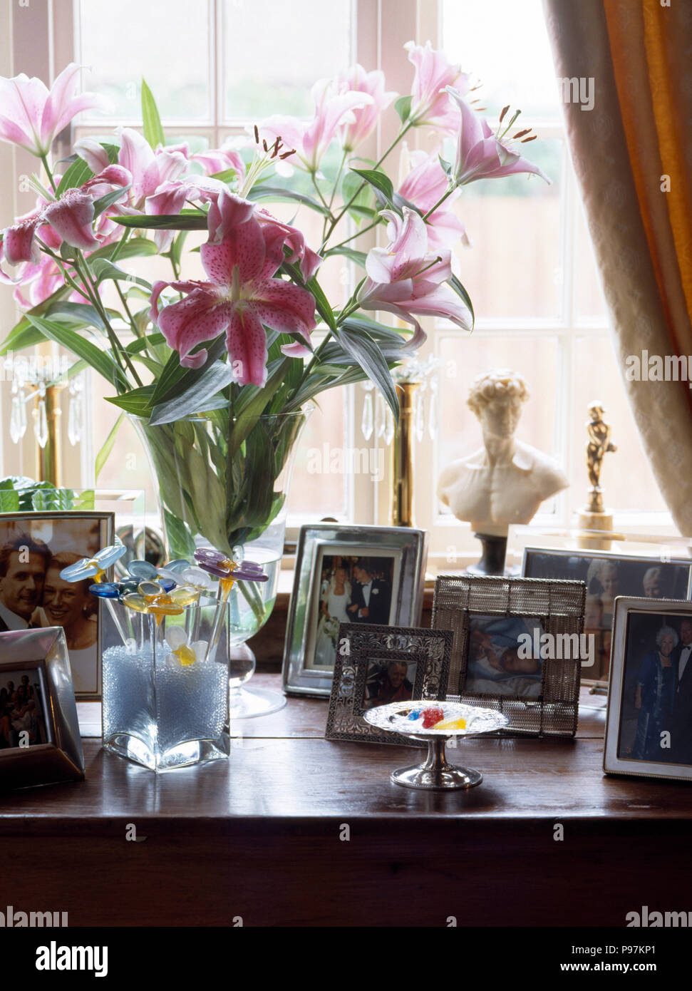 Vase of pink lilies and a collection of photographs on dressing table Stock Photo