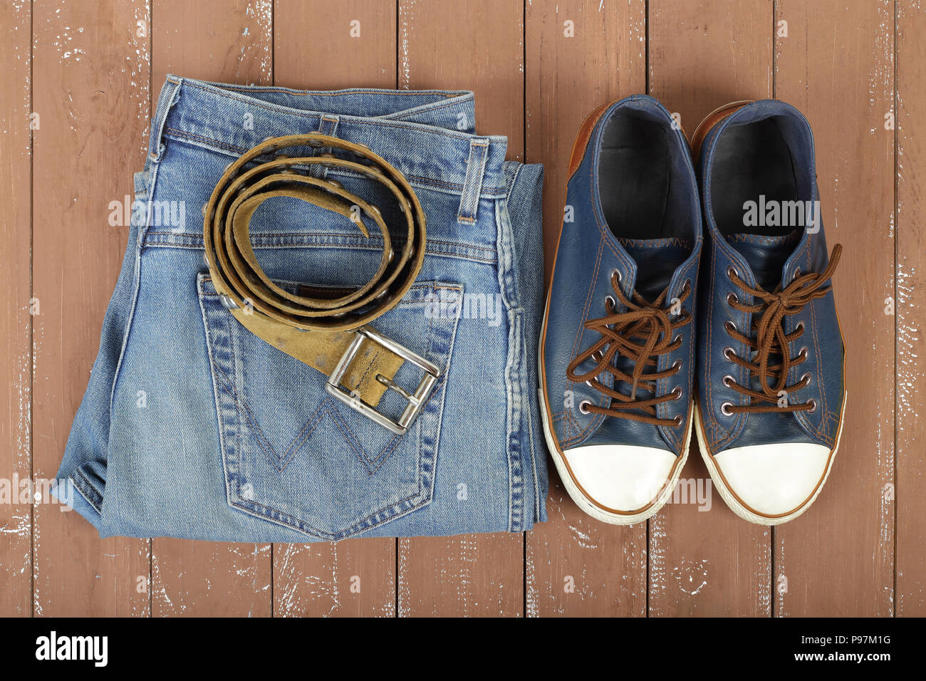 Clothes, shoes and accessories - Top view leather belt, gumshoes and blue jeans on a wooden background Stock Photo