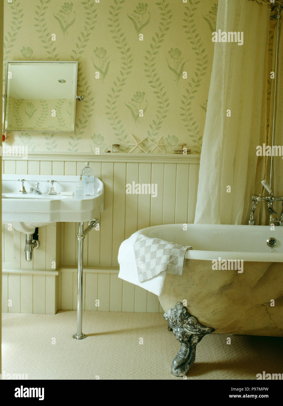 Paint effect marbled clawfoot bath in cream bathroom with wallpaper and panelling to dado height Stock Photo