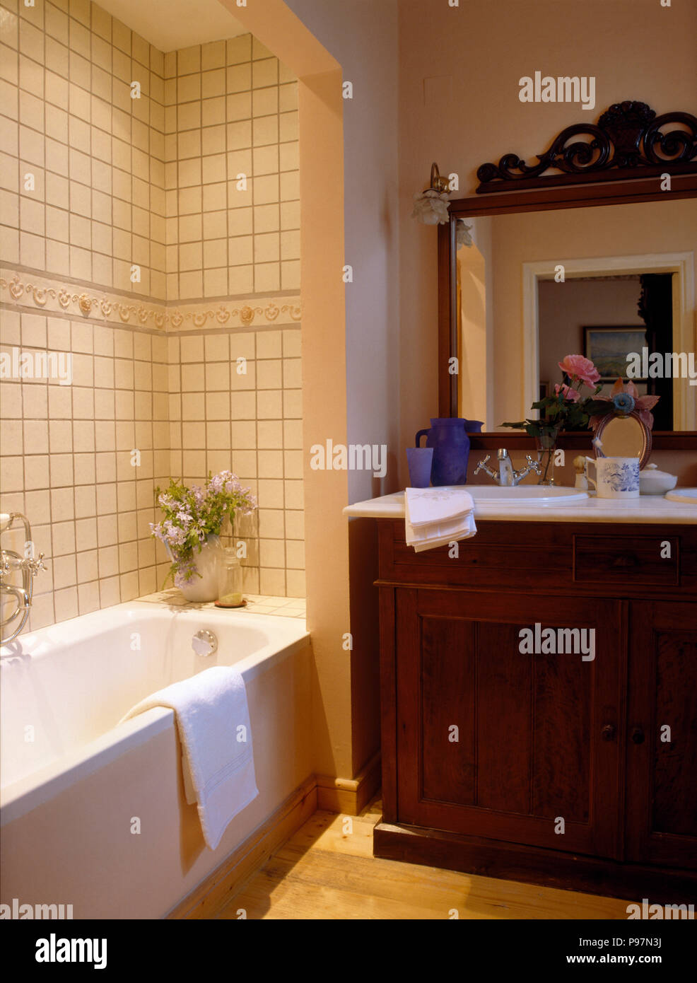 Cream tiles above recessed bath in a nineties bathroom with a mirror above fitted basin in vanity unit Stock Photo