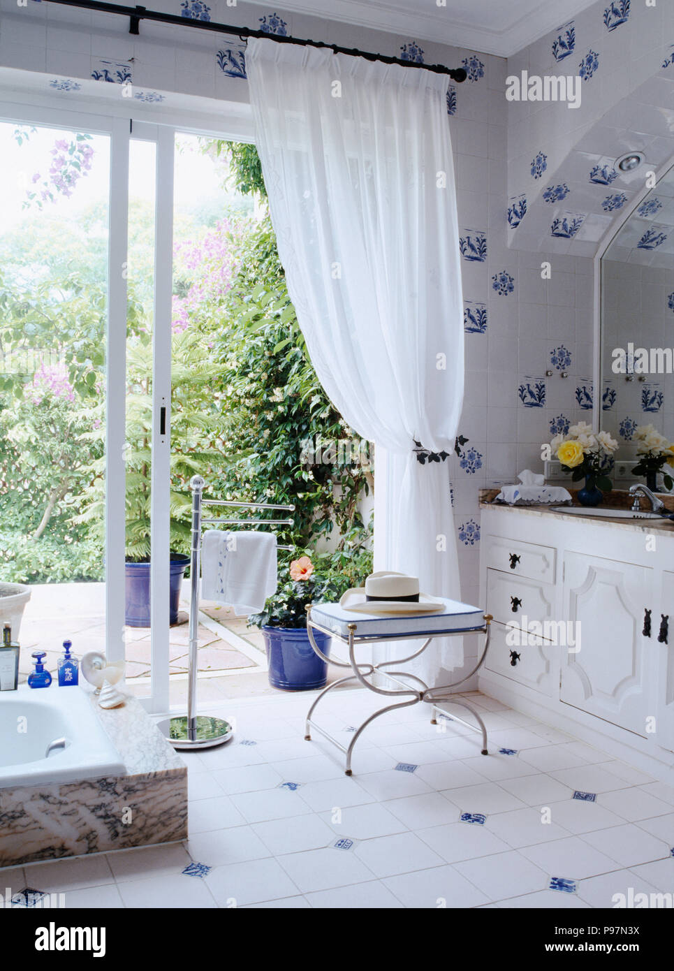 Blue+white ceramic tiled bathroom with white voile curtains on glass doors  to patio Stock Photo - Alamy