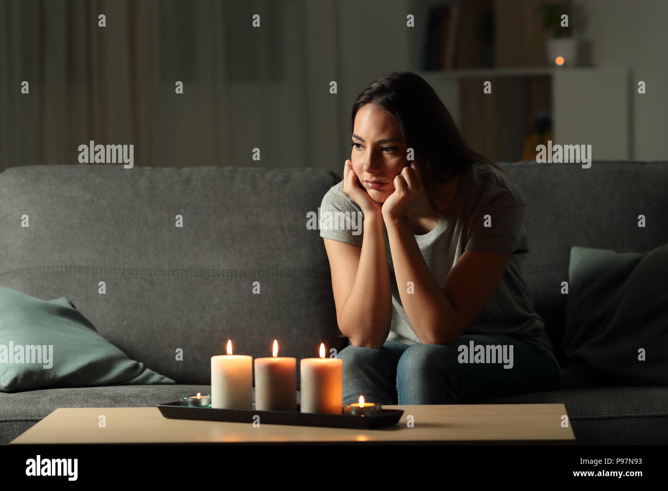 Frustrated woman sitting at home during a blackout sitting on a couch in the living room at home Stock Photo