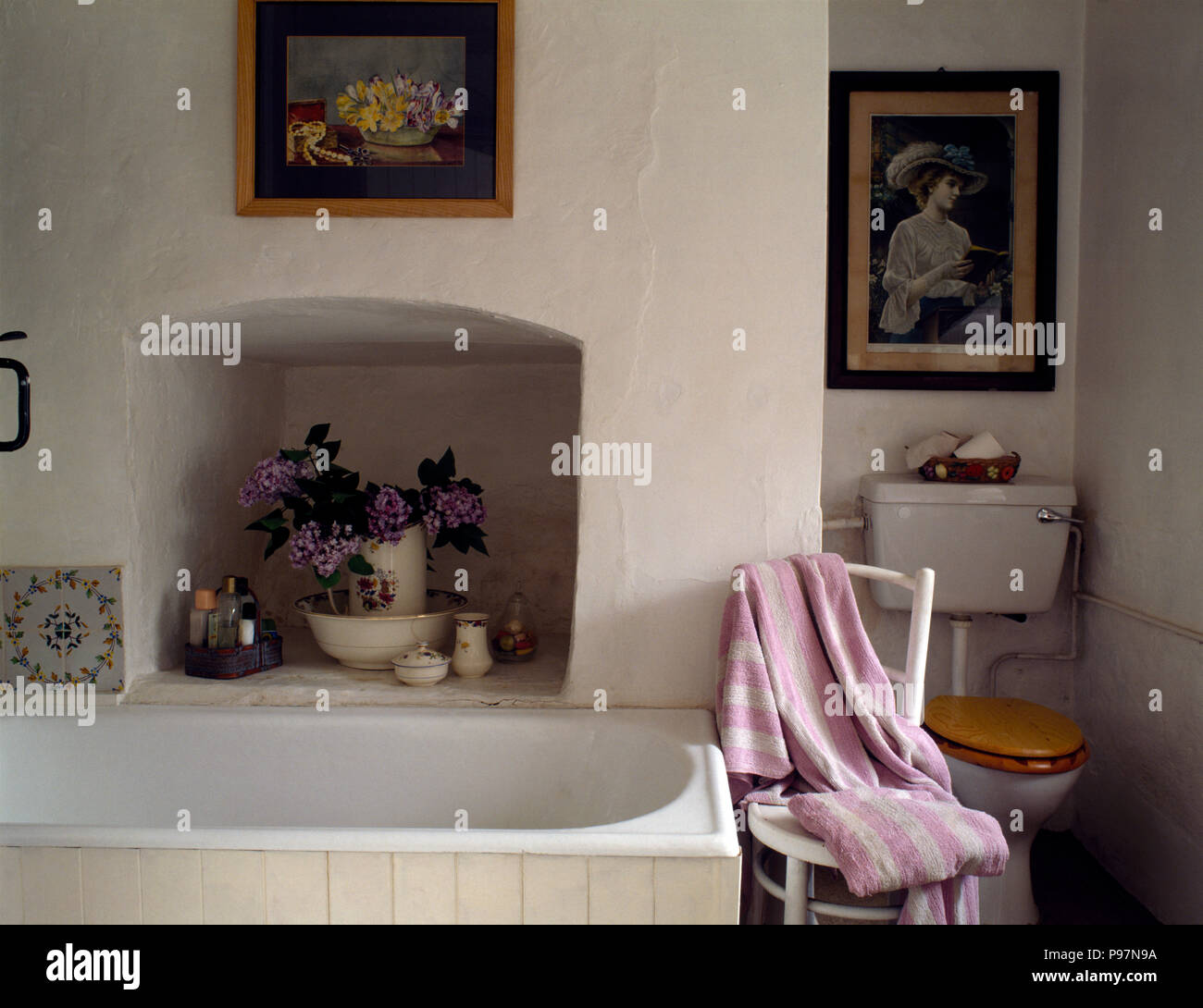 Jug of flowers in alcove above bath in a cottage bathroom Stock Photo