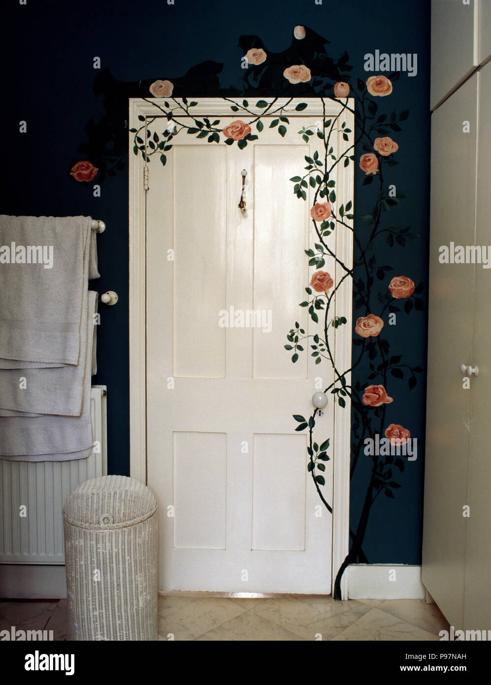 Roses painted around white door in dark blue nineties bathroom Stock Photo