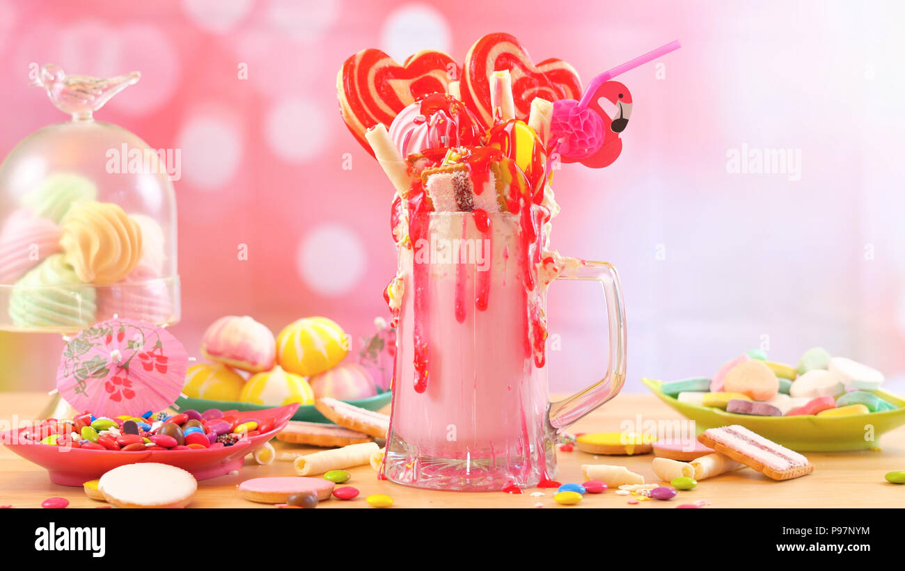 Making modern popular trend strawberry freak shakes milkshakes toppping with lollipops candy and cookies, selective focus. Stock Photo