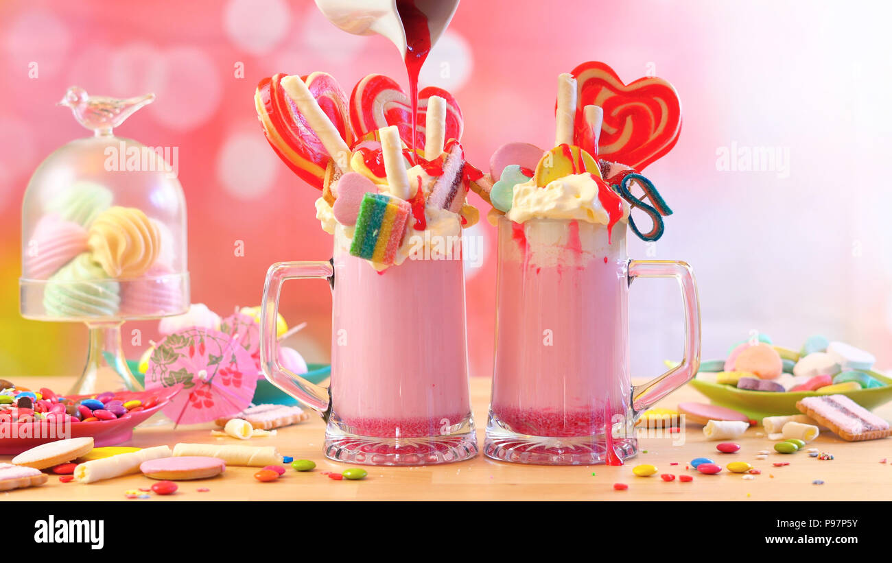 Making modern popular trend strawberry freak shakes milkshakes toppping with lollipops candy and cookies, selective focus. Stock Photo