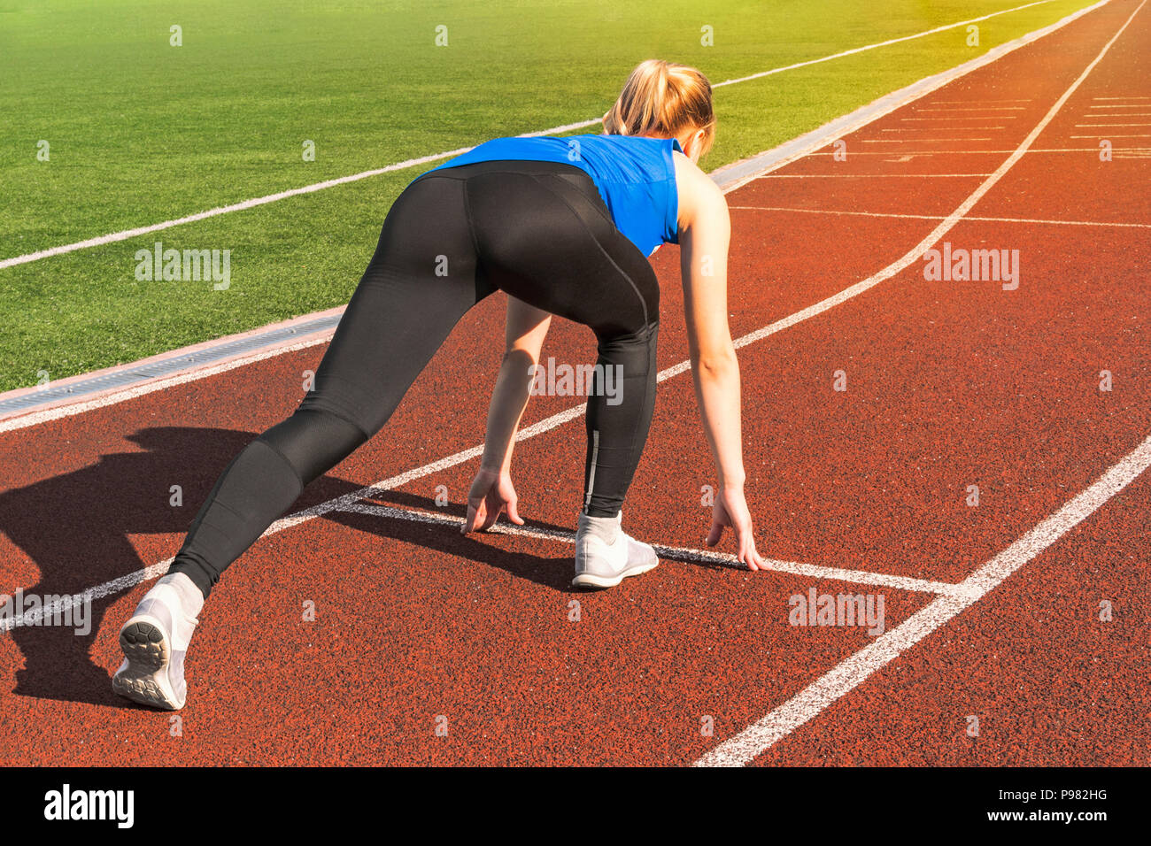 Teen Girl in the Starting Blocks at a Track Meet. Sports start. girl in pose on the starting line of treadmill. Active lifestyle. Concept of moving fo Stock Photo
